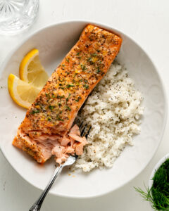 Salmon in a large white bowl with dill and lemon next to a side of white rice.