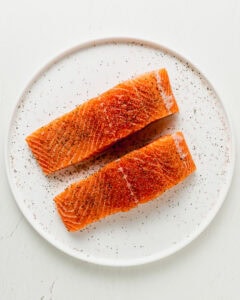 Salmon on a white plate sprinkled with salt and black pepper.