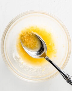 Melted butter in a small bowl with garlic powder and lemon zest. A spoon in stirring the mixture.