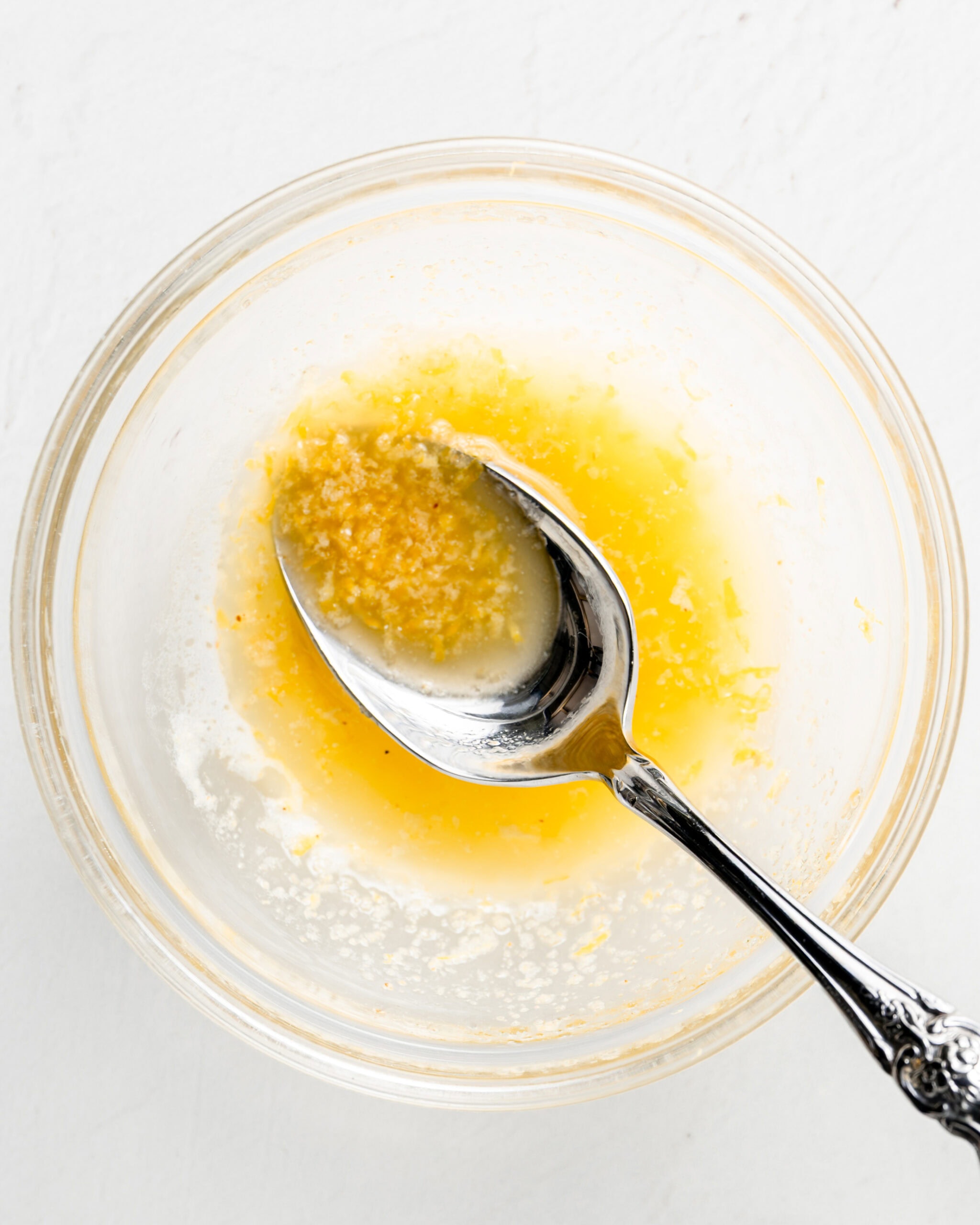 A small bowl of garlic butter with lemon zest. There is a spoon in the mixture.
