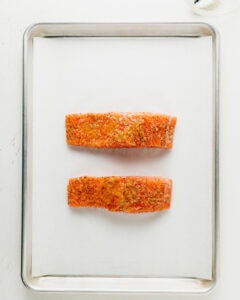 Salmon coated in seasonings and butter on a parchment paper lined baking sheet.