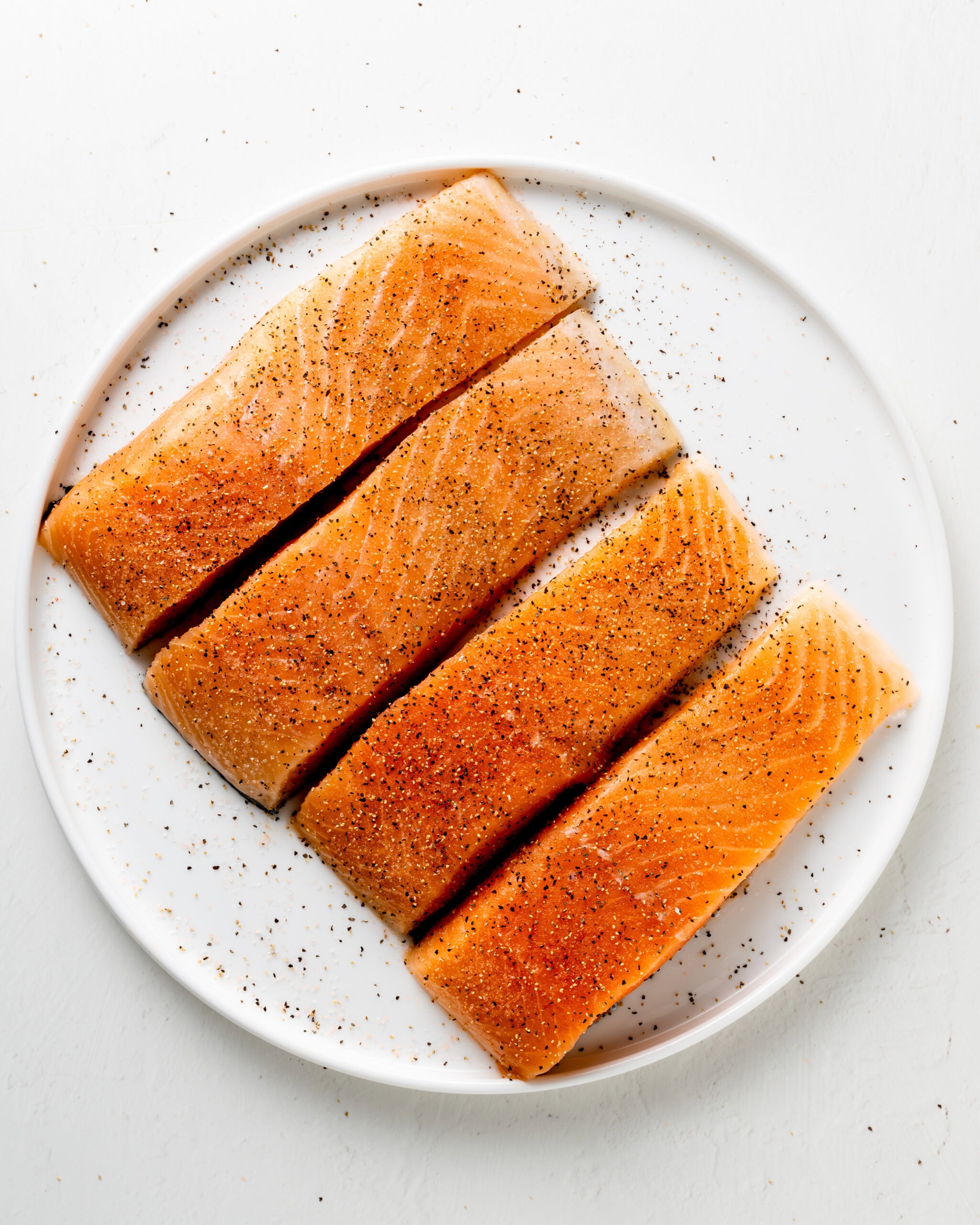 Salmon on a white plate seasoned with salt and black pepper.