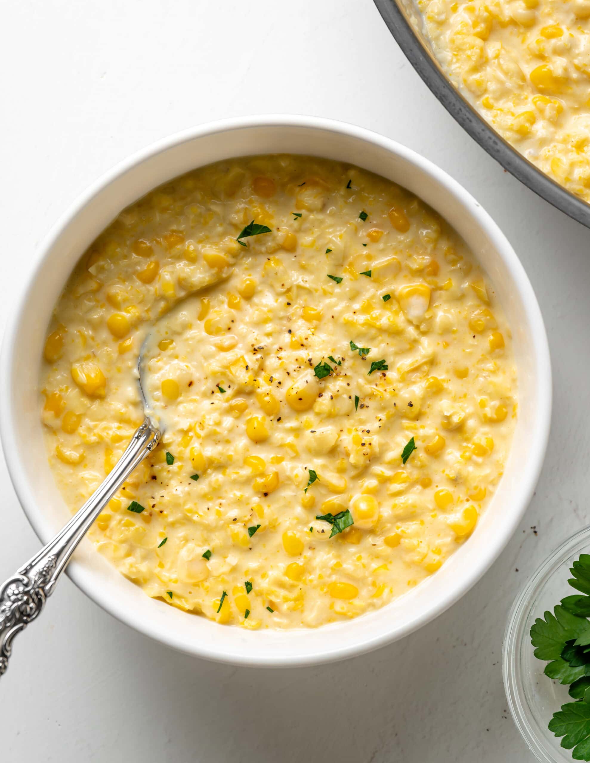 Gluten Free Creamed Corn in a white bowl with fresh herbs.