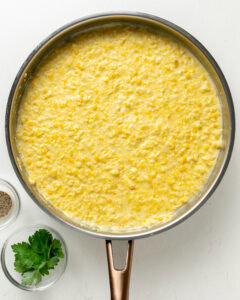 Creamed corn in a large skillet with herbs.