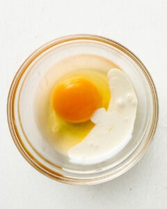 A egg with a splash of heavy cream in a glass bowl.