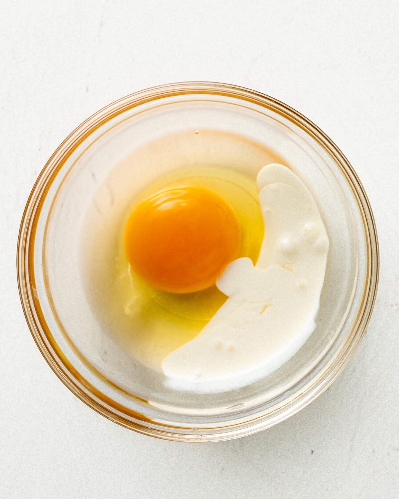 A egg with a splash of heavy cream in a glass bowl.
