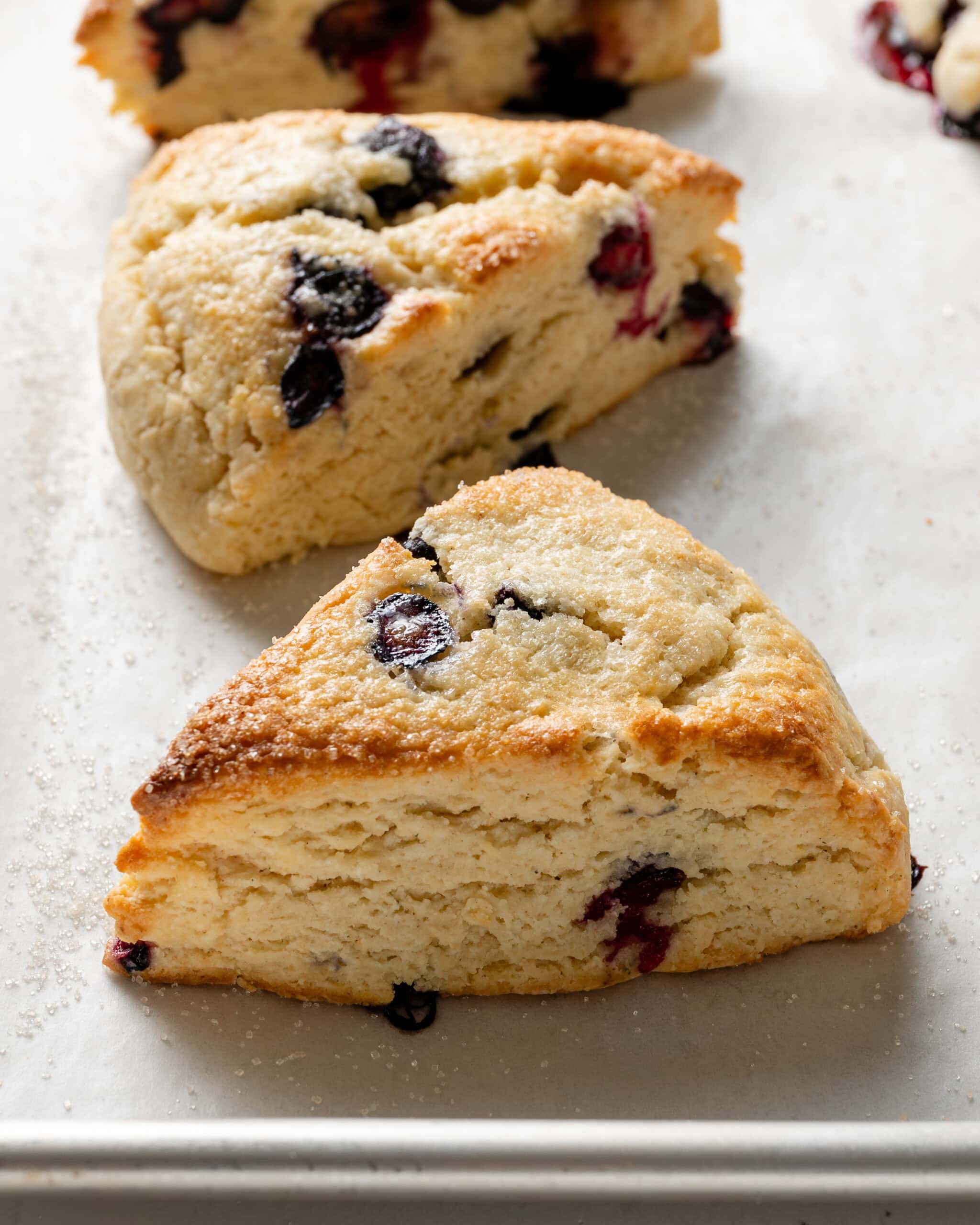 Blueberry scones with blueberries poking out of the sides and sugar glistened on top of the scones.