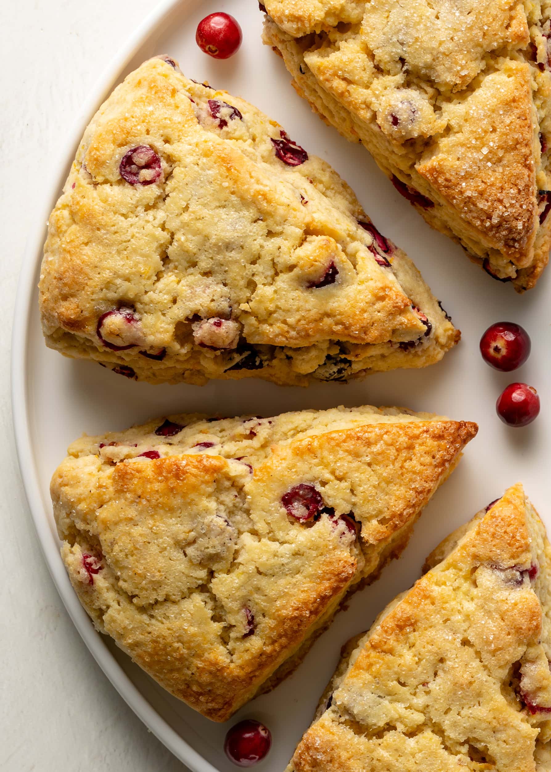 Gluten Free Cranberry Orange Scones on a white plate with fresh cranberries. 