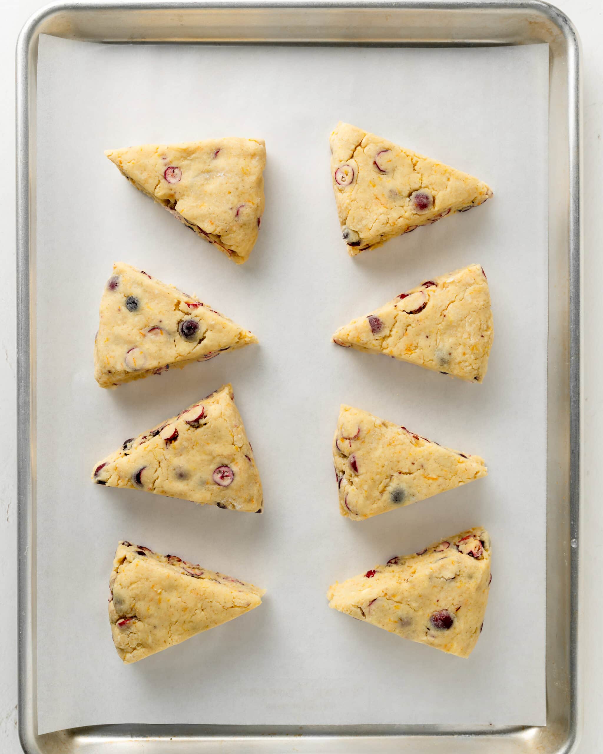 Cranberry orange scones on a baking sheet cut into eight triangles.