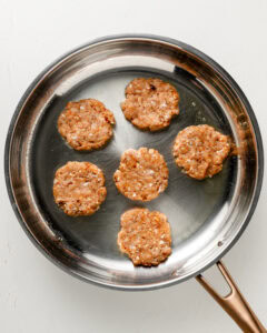 6 ground chicken breakfast sausage patties in a stainless steel skillet.