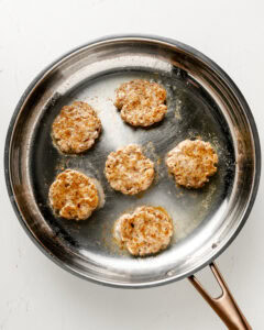 6 chicken breakfast sausages cooked in a stainless steel pan.