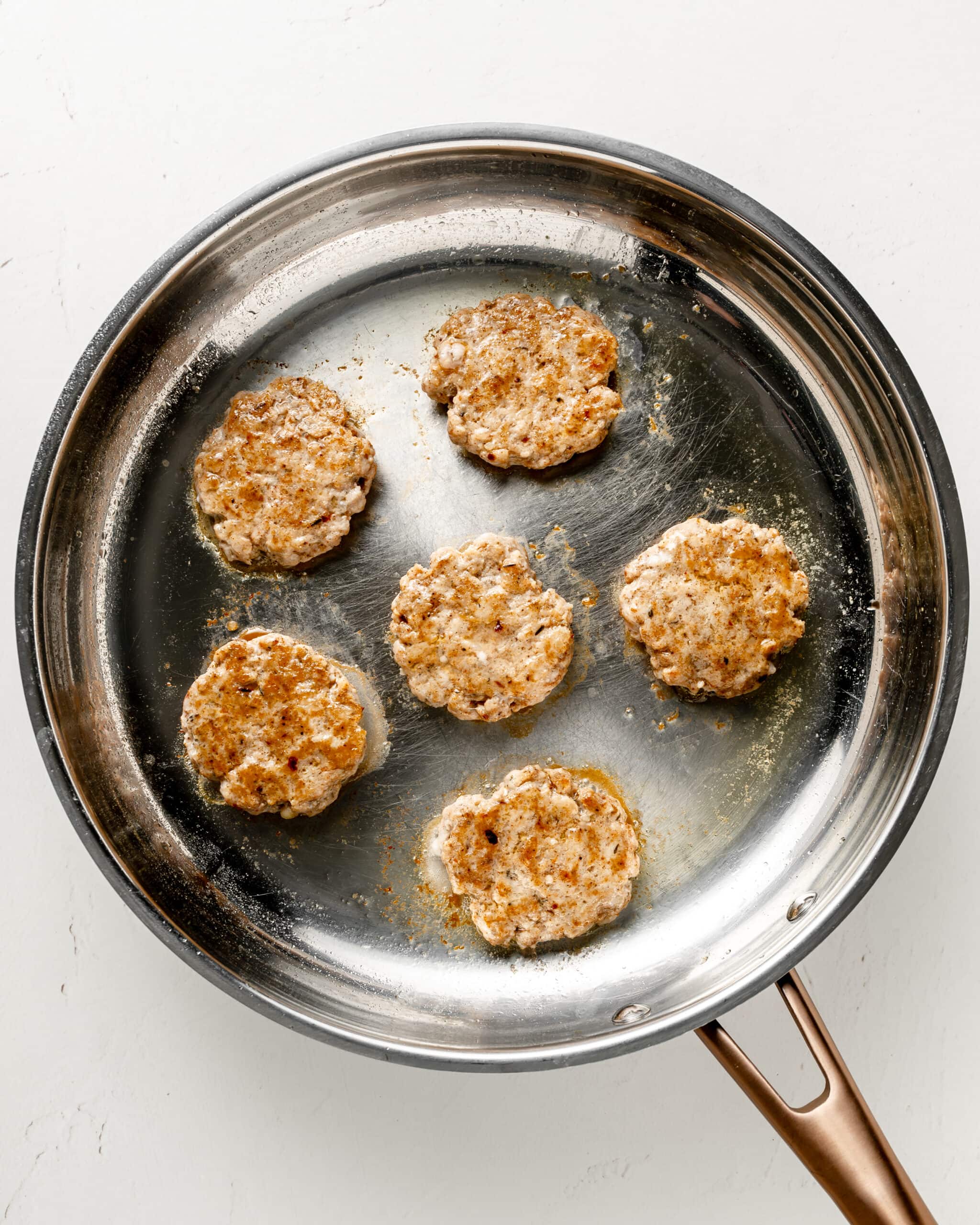Fully cooked chicken breakfast sausage patties in a stainless steel pan.