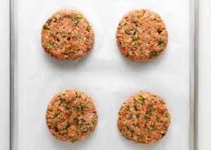 Four formed jalapeno turkey burger on lined baking sheet.