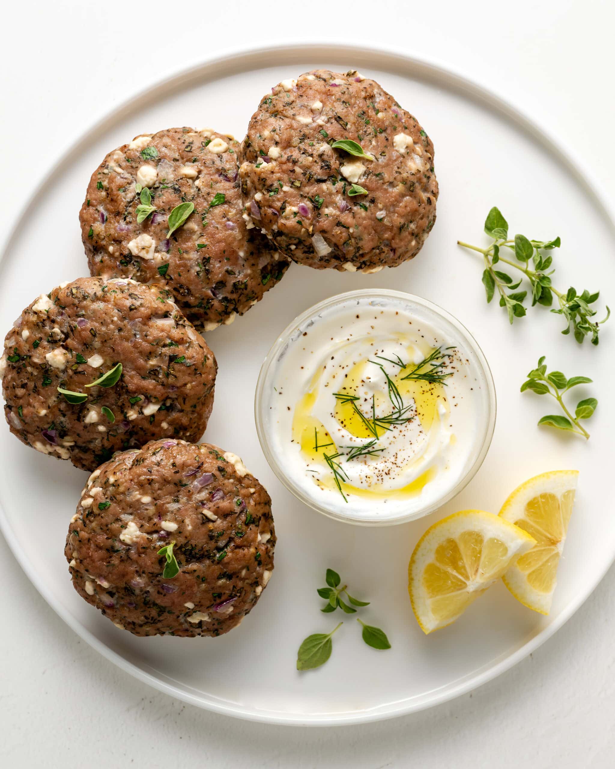 Mediterranean turkey burgers on a white plate with lemon and tzatziki sauce.