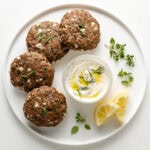Mediterranean-Turkey-Burgers On a White Plate With Tzatziki Sauce and Fresh Lemon Wedges.