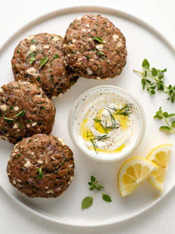 Mediterranean-Turkey-Burgers On a White Plate With Tzatziki Sauce and Fresh Lemon Wedges.