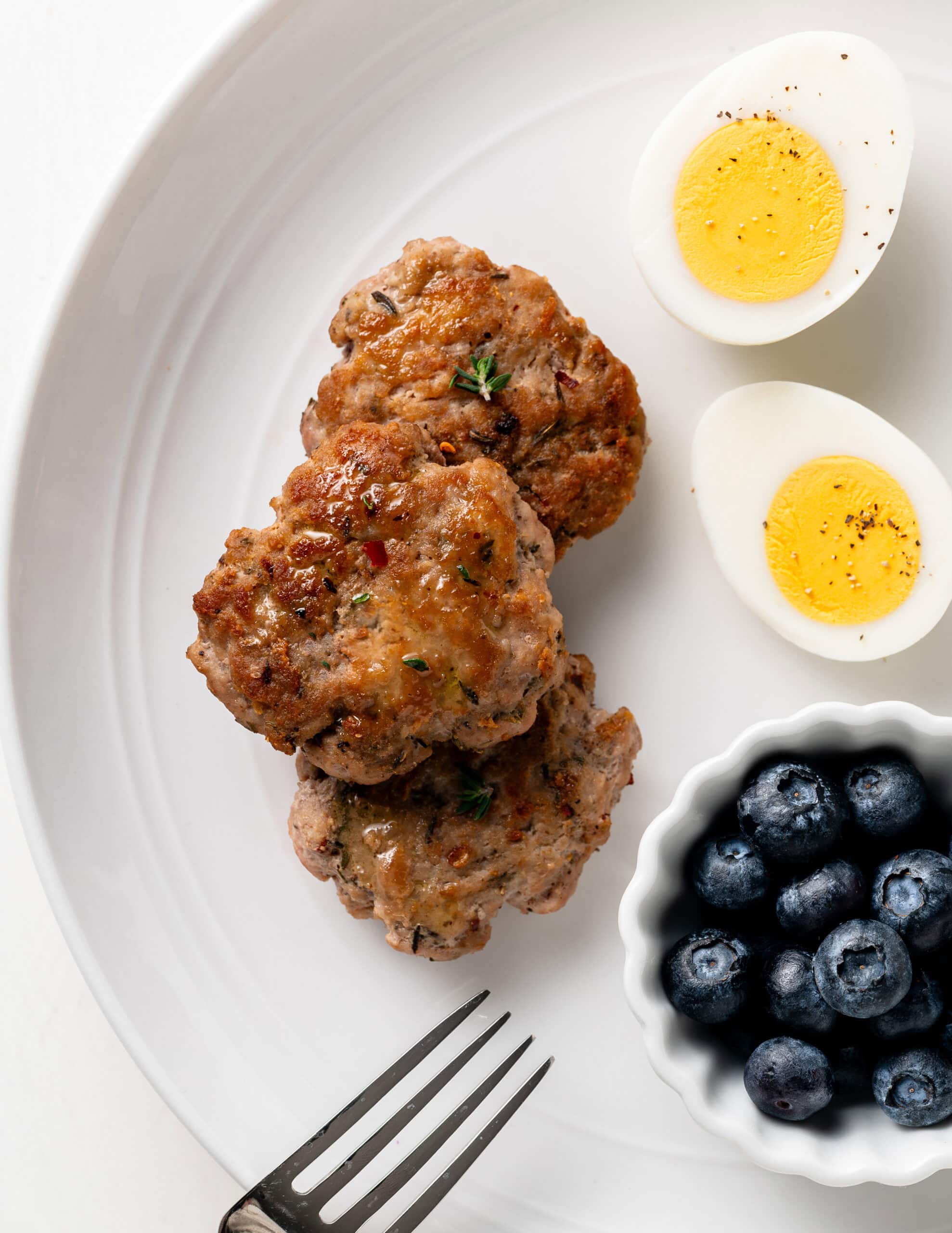 Three turkey sausage patties on a plate with a side of blueberries, and two hard boiled eggs.