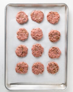 Ground turkey sausage patties on a parchment lined baking sheet.