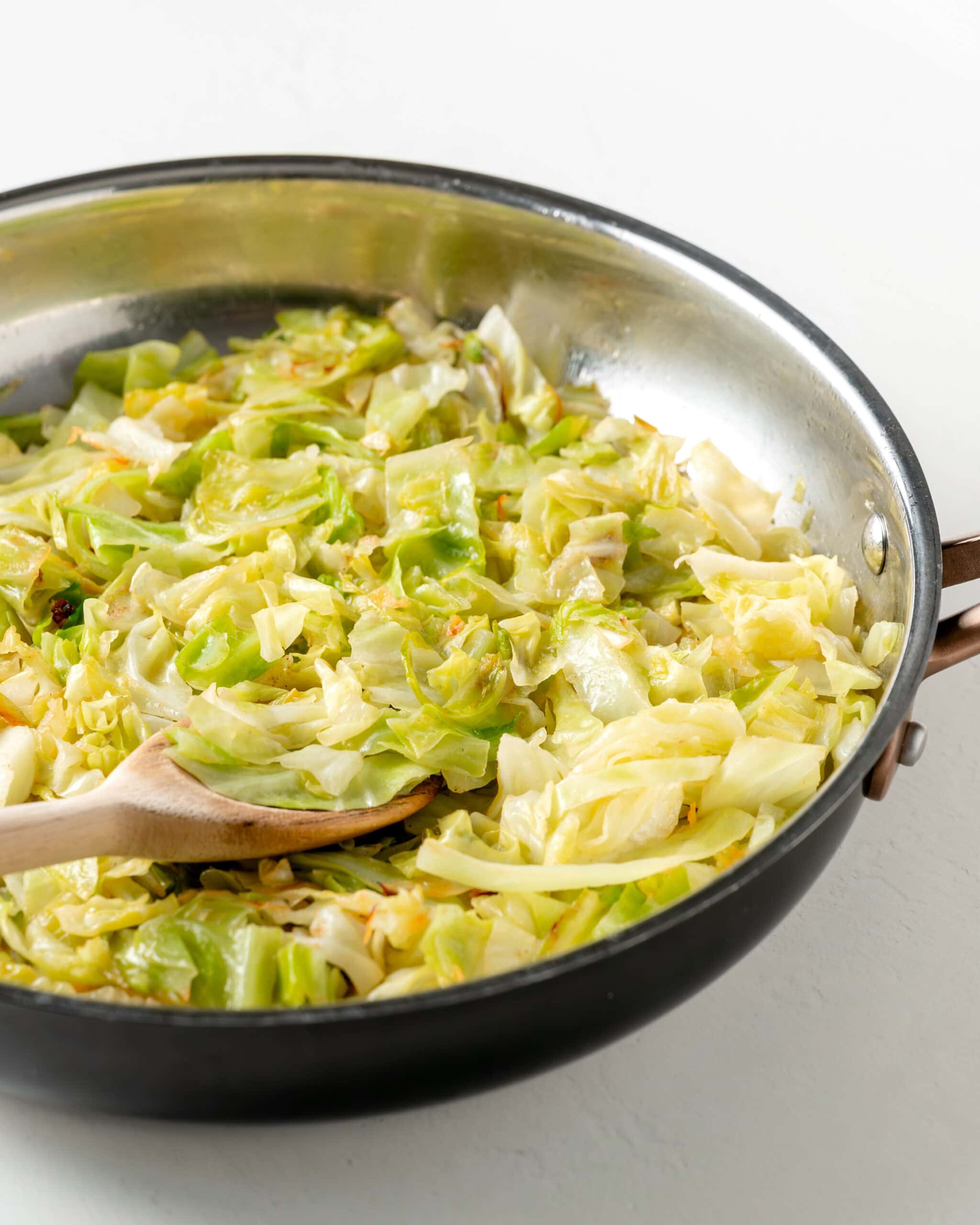 Side view on sauteed cabbage in a skillet with wooden spoon.