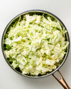 Add the green cabbage to a large skillet and saute.