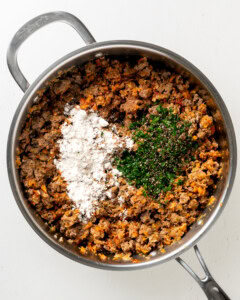 Adding gluten free flour and herbs to lamb mixture.