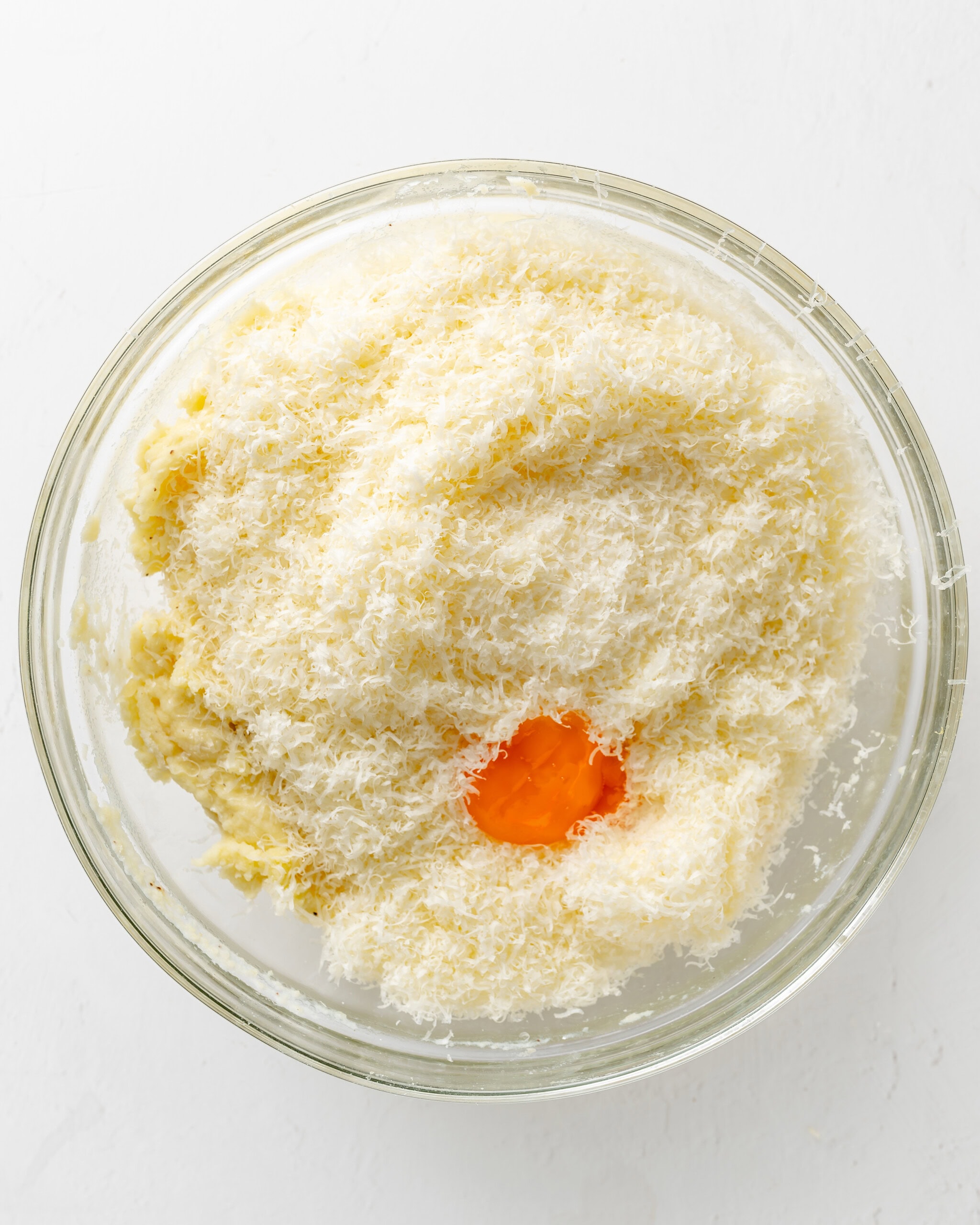 Adding egg yolk and cheese to mashed potatoes.