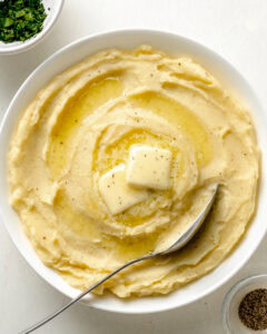 Yukon Gold Mashed Potatoes in a large white bowl with two slices of butter.