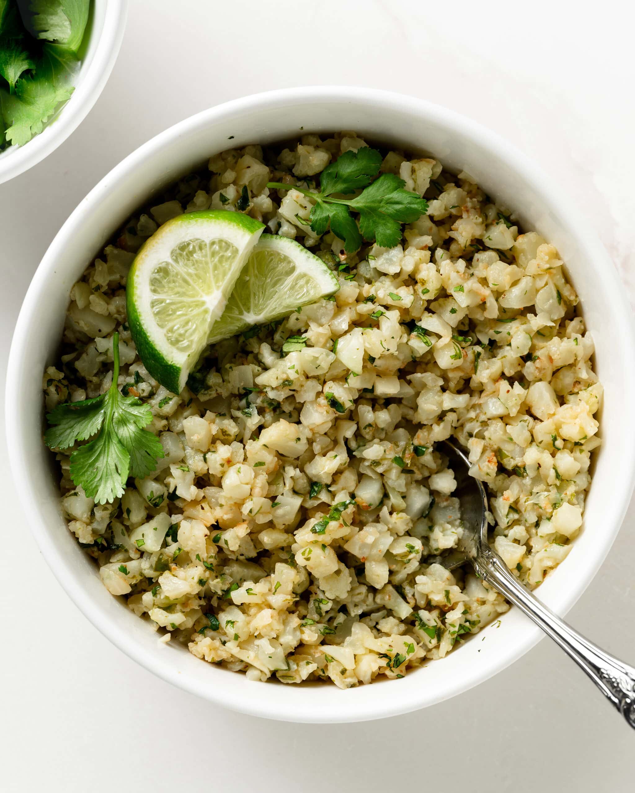 Cauliflower Lime Rice in a white bowl with cilantro leaves and limes. 
