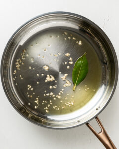 Bay leaf in a stainless steel pain with minced garlic.