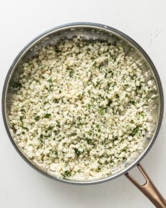 Cauliflower rice with added lime juice, zest and fresh cilantro in a stainless steel pan.