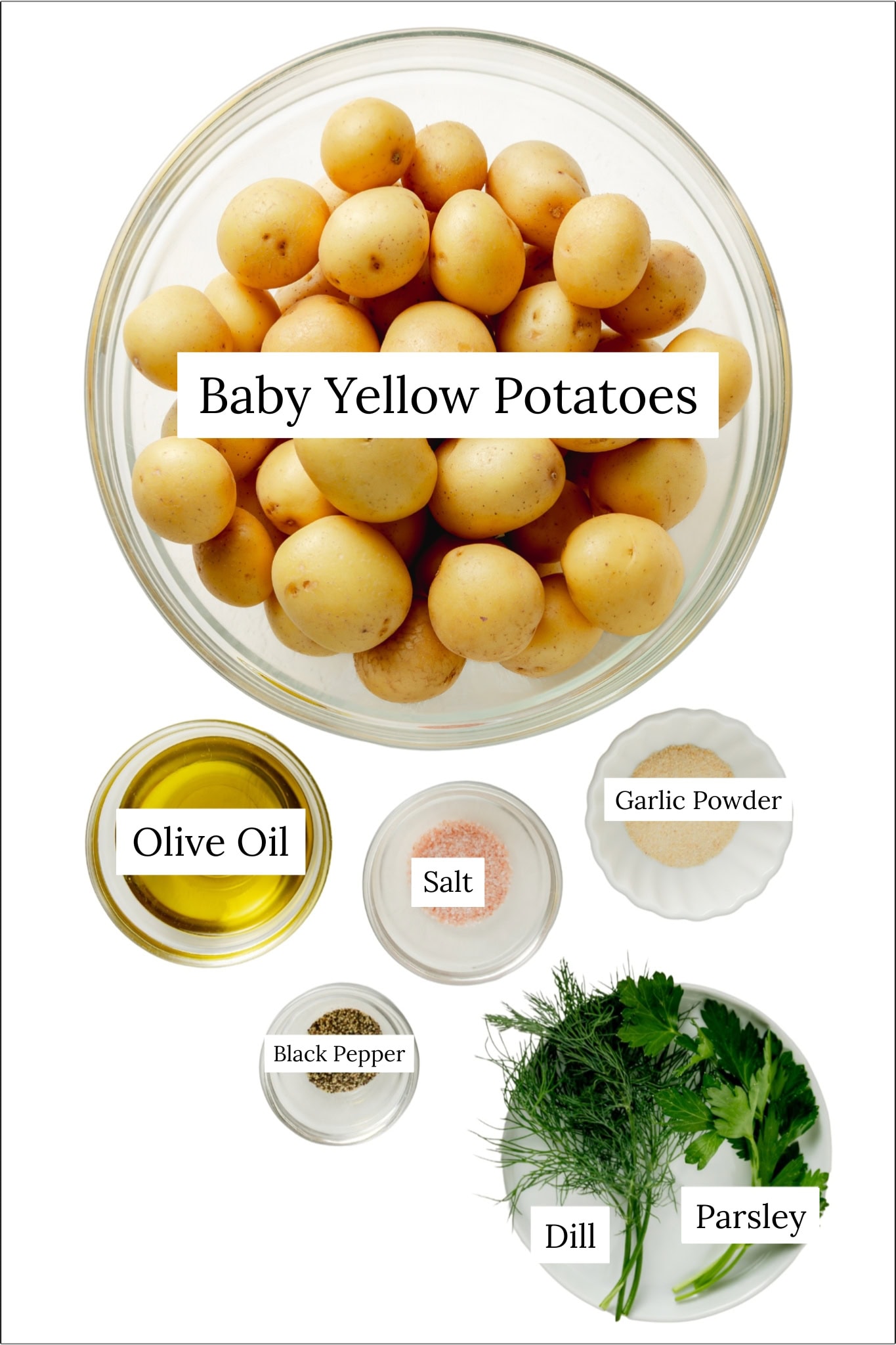 Recipe ingredients for dill roasted potatoes. A large clear bowl of yellow baby potatoes, olive olive, salt, garlic powder, black pepper, fresh dill, and fresh parsley.