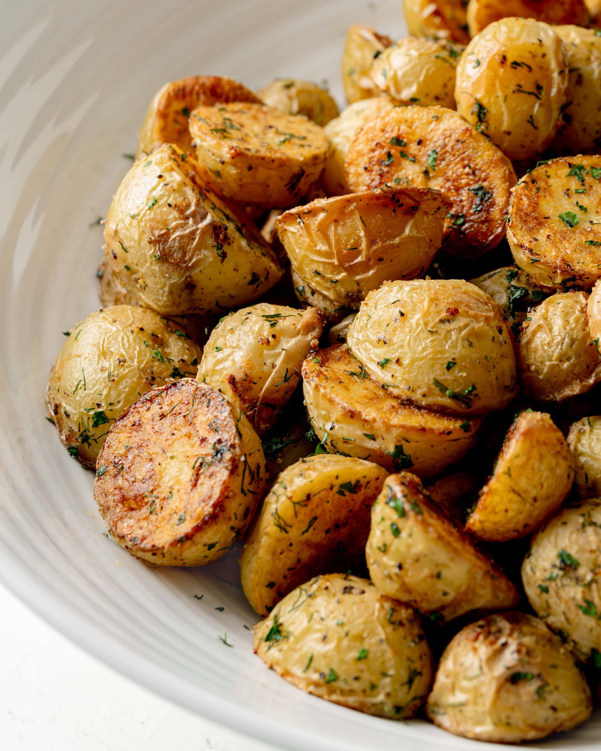 Side view of crispy garlic dill roasted potatoes, in a large white serving bowl.