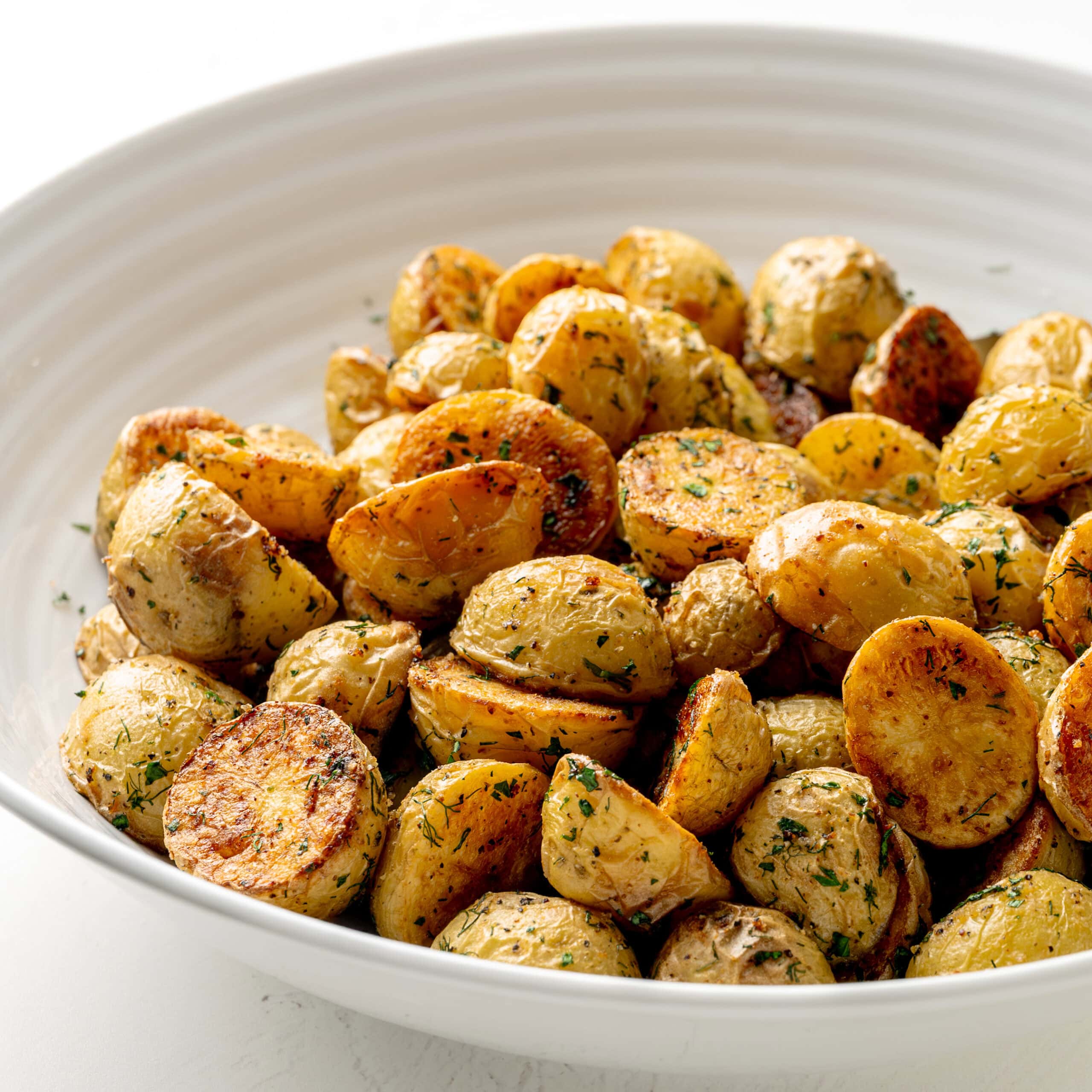 Side view of crispy garlic dill roasted potatoes, in a large white serving bowl.